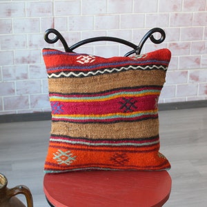 May include: A colorful striped throw pillow with a geometric pattern. The pillow is made of woven fabric and has a brown, red, orange, blue, and yellow color scheme.