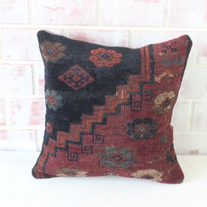 Puede incluir: Una almohada de tiro con estampado negro y rojo con un dise&ntilde;o geom&eacute;trico. La almohada est&aacute; hecha de una tela suave y tejida y tiene un borde con flecos.