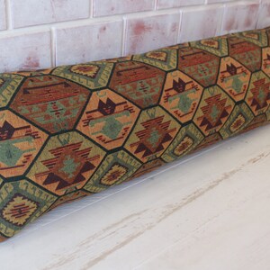 May include: A long, rectangular pillow with a geometric pattern in shades of brown, green, orange, and red. The pattern is made up of hexagons and stars.