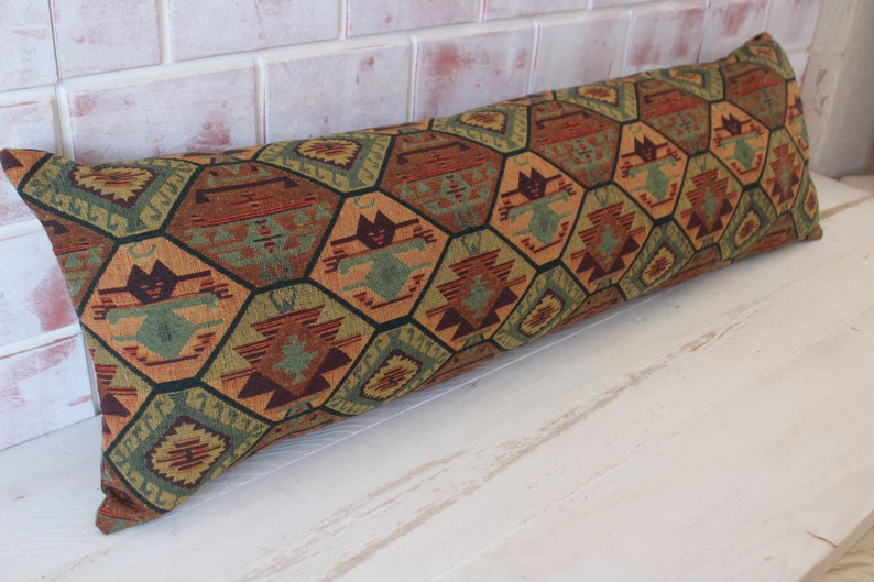 May include: A long, rectangular pillow with a geometric pattern in shades of brown, green, orange, and red. The pattern is made up of hexagons and stars.