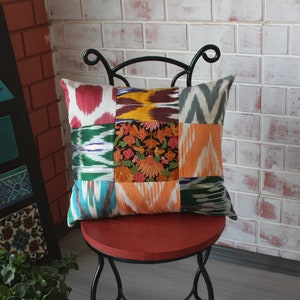 Könnte beinhalten: Ein farbenfrohes Patchwork-Kissen mit Blumenmuster sitzt auf einem schwarzen Metallstuhl mit roter Sitzfläche. Der Stuhl steht vor einer weißen Backsteinwand.