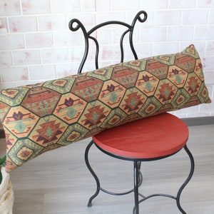 May include: A long, rectangular pillow with a geometric pattern in shades of green, brown, and orange. The pillow is resting on a black metal chair with a red seat.