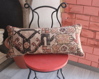 May include: A long, rectangular pillow with a beige background and a colorful geometric pattern in shades of brown, red, and cream. The pillow is sitting on a black metal chair with a red seat.