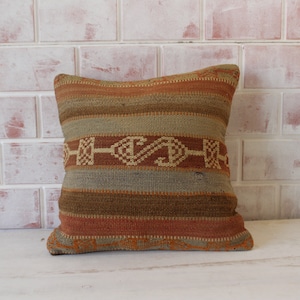 May include: A decorative throw pillow with a woven pattern in shades of brown, beige, and orange. The pillow has a geometric design with a central motif of a stylized 'S' shape.