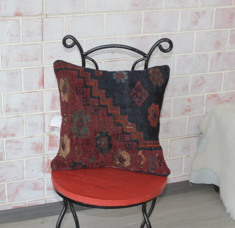 Puede incluir: Un coj&iacute;n de tiro rojo, negro y verde con dise&ntilde;os intrincados se sienta en un taburete de metal rojo. El coj&iacute;n est&aacute; hecho de una tela suave y tejida y tiene un aspecto vintage &uacute;nico.
