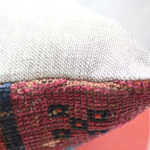 Puede incluir: Primer plano de una almohada con una funda de tela de lino beige y un patr&oacute;n tejido colorido en el borde inferior.