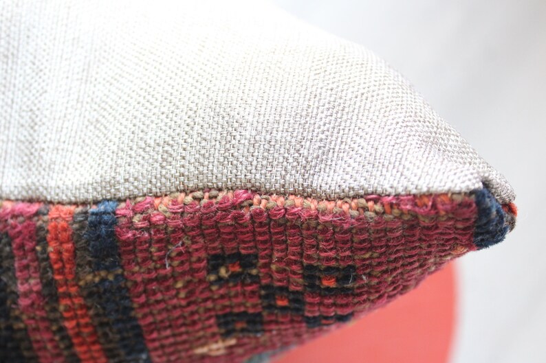 Puede incluir: Primer plano de una almohada con una funda de tela de lino beige y un patr&oacute;n tejido colorido en el borde inferior.