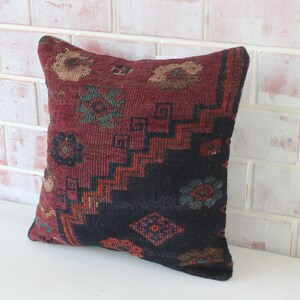 Puede incluir: Una almohada de tiro roja, negra y azul con un dise&ntilde;o geom&eacute;trico. La almohada est&aacute; hecha de tela tejida y tiene un borde con flecos.