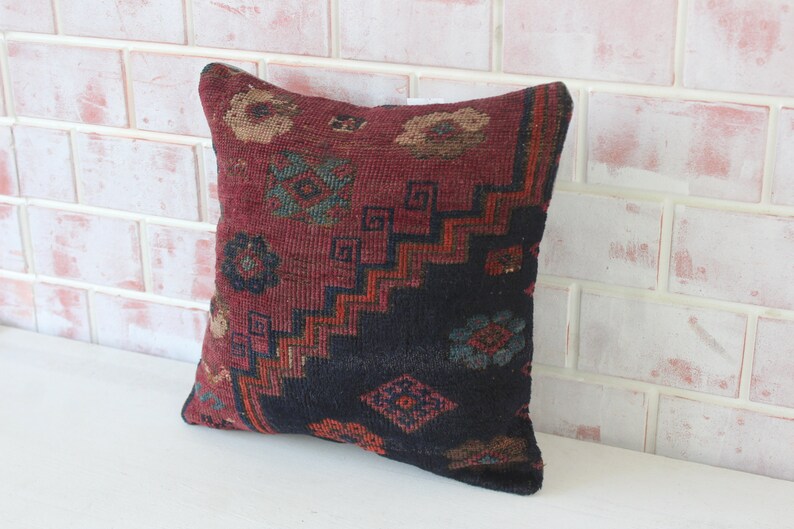 Puede incluir: Una almohada de tiro roja, negra y azul con un dise&ntilde;o geom&eacute;trico. La almohada est&aacute; hecha de tela tejida y tiene un borde con flecos.