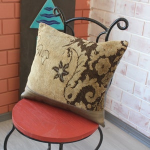 May include: A decorative pillow with a brown and beige floral pattern. The pillow is sitting on a red chair with a black metal frame.
