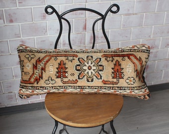 May include: A long, rectangular pillow with a beige background and a colorful, intricate pattern. The pillow is made of woven fabric and has a fringed edge.