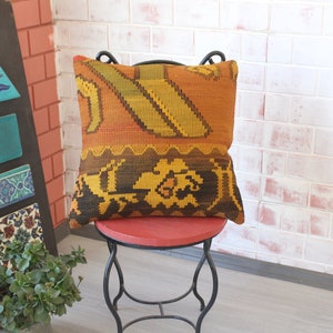 May include: A colorful, patterned throw pillow with a woven design in shades of orange, yellow, brown, and black. The pillow is sitting on a red metal stool.