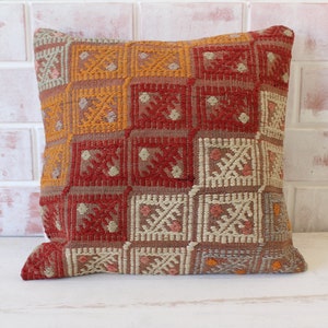 May include: A square cushion with a geometric pattern in shades of red, orange, beige, and white.