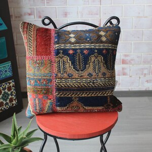 May include: A colorful patchwork pillow with a blue, brown, and red geometric pattern. The pillow is sitting on a red stool with a black metal frame.