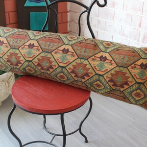 May include: A long, rectangular pillow with a geometric pattern in shades of green, brown, orange, and red. The pillow is resting on a red chair with a black metal frame.
