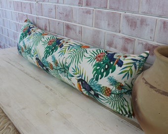 May include: A long, white bolster pillow with a tropical print featuring toucans, pineapples, and green leaves. The pillow is lying on a white wooden surface.
