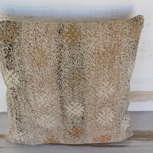 May include: A square, textured pillow with a neutral color palette. The pillow features a woven design with cream, brown, and tan hues. The pillow's surface has a raised, tactile quality, adding visual interest and depth. This decorative pillow is suitable for home decor.