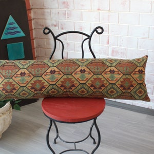 May include: A long, rectangular pillow with a geometric pattern in shades of brown, green, and orange. The pillow is resting on a red chair with a black metal frame.