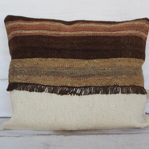 以下が含まれることがあります： フリンジの縁取りが施された、茶色とベージュのストライプの投げ枕。枕は織物で作られており、白い裏地があります。