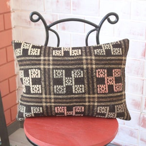 May include: A brown and white patterned throw pillow with pink accents sits on a red chair. The pillow has a geometric design and is made of a soft, woven fabric.