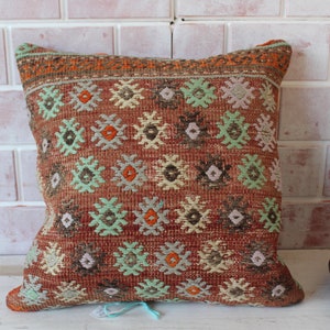 Peut inclure: Un coussin de décoration rouge, vert et crème avec un motif géométrique. Le coussin est en tissu tissé et a une bordure frangée.