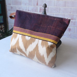 May include: A rectangular pouch with a brown and white chevron pattern on the bottom half. The top half is a deep burgundy color with a yellow and pink stripe. It has a brown leather handle.