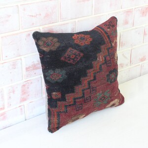 Puede incluir: Una almohada decorativa con un patr&oacute;n geom&eacute;trico negro, rojo y verde. La almohada est&aacute; hecha de una tela suave y tejida y tiene un borde con flecos.