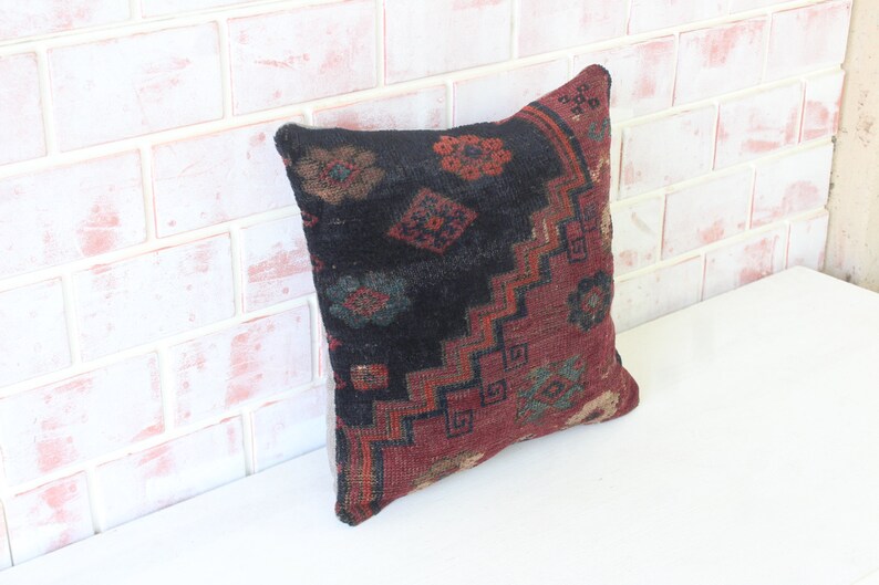Puede incluir: Una almohada decorativa con un patr&oacute;n geom&eacute;trico negro, rojo y verde. La almohada est&aacute; hecha de una tela suave y tejida y tiene un borde con flecos.