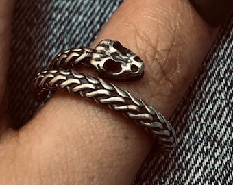 Peut inclure: Une bague en argent en forme de serpent avec un design détaillé de tête de serpent. La bague est portée sur un doigt avec un vernis à ongles noir.