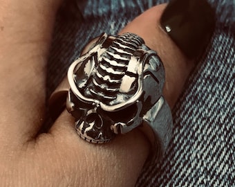 Peut inclure: Une bague en argent en forme de crâne avec des détails complexes. La bague est portée sur un doigt avec un vernis à ongles noir.