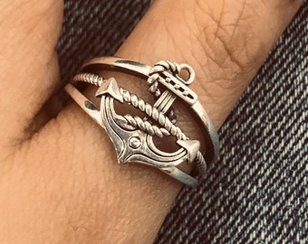 Puede incluir: Un anillo de plata con un diseño de ancla y detalles de cuerda. El anillo se lleva en un dedo con esmalte de uñas negro.