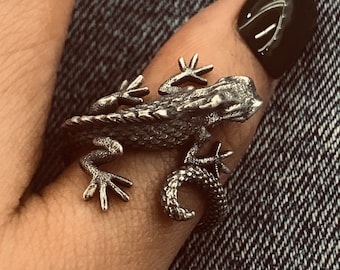 Puede incluir: Un anillo de plata con forma de lagarto en un dedo con esmalte de uñas negro.