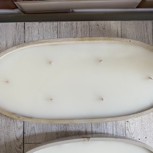 May include: A white oval concrete candle holder with five wicks. The holder is on a wooden surface.