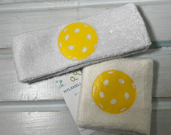 May include: Two white sweatbands with yellow pickleball designs. The sweatbands are made of a soft, absorbent material and are perfect for keeping your wrist dry during a game.