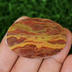 May include: A close-up of a yellow, red, and brown agate cabochon. The stone has a swirling pattern of colors and is smooth and polished.