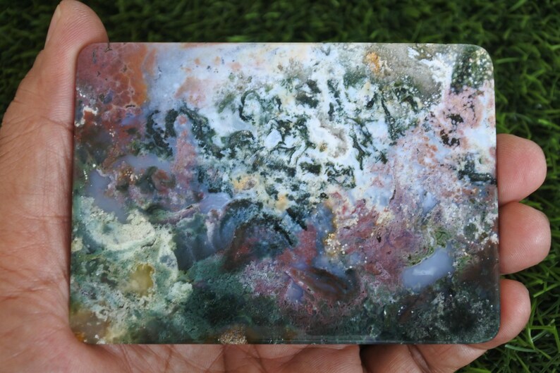 May include: A rectangular polished slab of moss agate featuring a complex pattern of translucent white, deep forest green, earthy brown, and soft pink inclusions. The stone displays a smooth, flat surface with natural mineral dendrites.