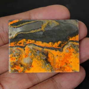Peut inclure: Une pierre précieuse rectangulaire avec un motif saisissant d'orange, de jaune, de gris et de noir. La pierre est tenue dans une main, mettant en valeur ses couleurs et textures naturelles. Idéal pour la joaillerie ou la collection.