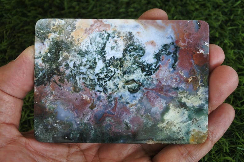 May include: A rectangular slab of polished moss agate featuring a complex, organic pattern of deep forest green, earthy terracotta red, creamy white, and translucent grey inclusions throughout the smooth, flat stone surface.