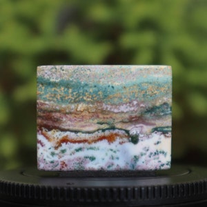 May include: A polished slab of green, brown, white, and pink agate with a layered pattern. The agate is a natural stone with a smooth surface.
