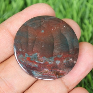 May include: A round, polished, red, brown, and green agate cabochon with a swirling pattern.