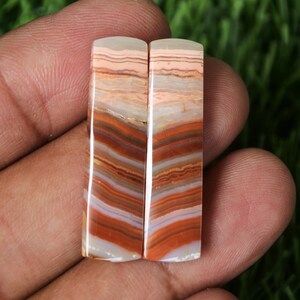 May include: Two rectangular cabochons of banded agate with a mix of white, brown, and orange colors. The cabochons are cut and polished.