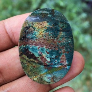 May include: Oval-shaped gemstone with a unique pattern of teal, brown, and rust colors. The stone has a polished surface and a natural, earthy appearance. The gemstone is a beautiful example of natural stone art.