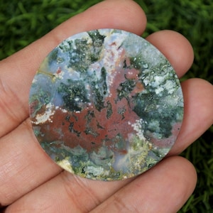 May include: A round, polished, green, white, and red agate stone with a swirling pattern. The stone is approximately 5 cm in diameter.