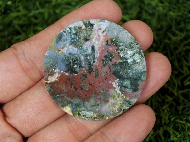 May include: A round, polished, green, white, and red agate stone with a swirling pattern. The stone is approximately 5 cm in diameter.