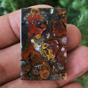 Op de afbeelding: Een rechthoekige, gepolijste agaat cabochon met een kleurrijk, abstract patroon van rood, oranje, geel, bruin en zwart. De agaat heeft een gladde, glanzende afwerking.