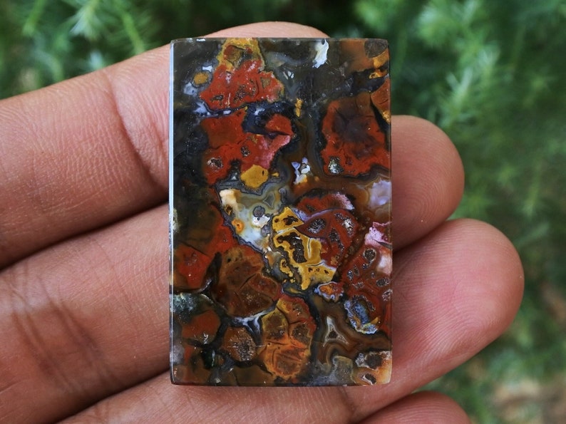 Op de afbeelding: Een rechthoekige, gepolijste agaat cabochon met een kleurrijk, abstract patroon van rood, oranje, geel, bruin en zwart. De agaat heeft een gladde, glanzende afwerking.