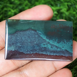 May include: A rectangular green, blue, and brown gemstone cabochon with a polished finish. The stone has a layered appearance with a darker brown layer at the bottom and a lighter green layer at the top.
