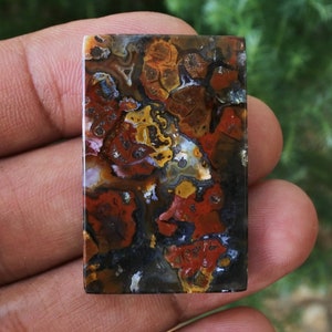 Op de afbeelding: Een rechthoekige, gepolijste agaat cabochon met een kleurrijk, abstract patroon van rood, oranje, geel, bruin en zwart. De agaat heeft een gladde, glanzende afwerking.