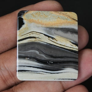 May include: A rectangular, polished stone with a layered pattern of black, white, and brown. The stone has a smooth, glossy finish.