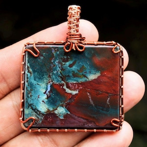 Puede incluir: Un colgante envuelto en alambre de cobre con una piedra de ágata cuadrada roja, azul y verde.
